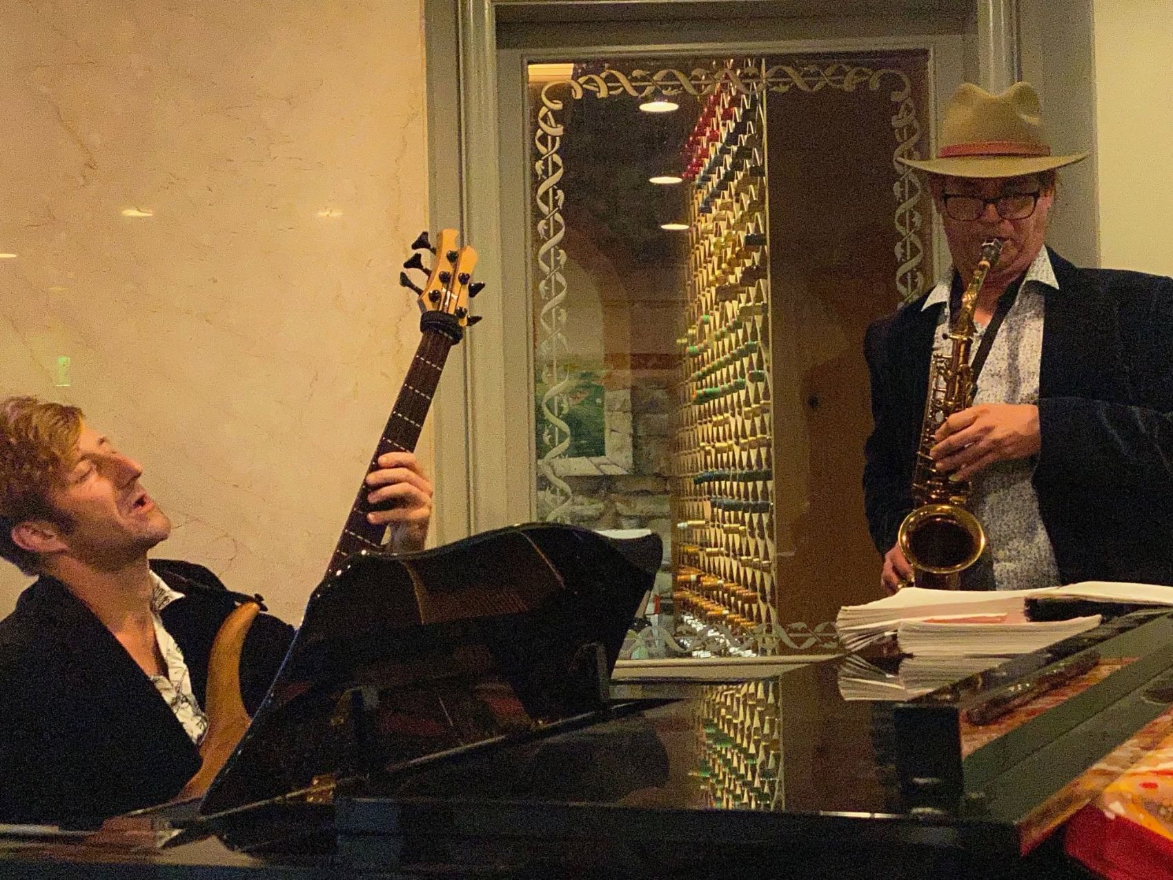 Dan in a hat, saxophone by the wine wall, pianist singing